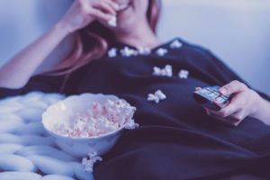 Woman lying down eating popcorn with a remote