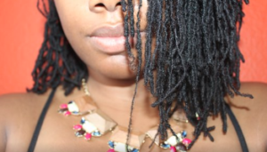 Bottom half of black woman's face with dreads hanging down on one shoulder.