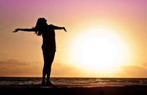 Silhouette of woman with arms out greeting the sun.