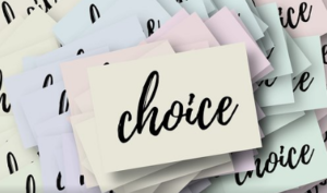 A pale yellow sticky note sitting on top of a pile of pastel sticky notes with the word choice on them in cursive writing.