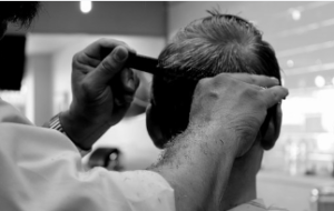 Male barber giving a client a haircut with comb and scissors.