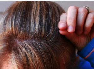 Female pulling a grey hair from blonde highlighted hair.