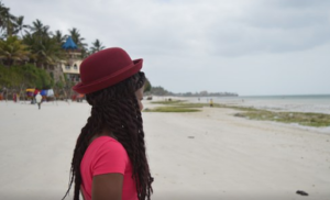 Lady in a bright pink blouse with long dark hair wearing a burgundy red hat looking out to sea.