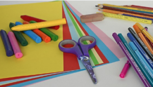 A pile of different coloured cartridge paper, crayons, eraser and cutting shears etc. on a table.