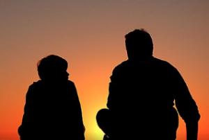 Parent and child talking watching the sun set in silhouette.