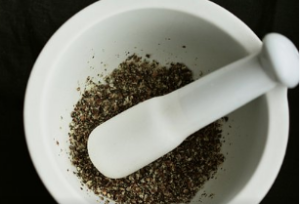 White mortar with a white pestle and ground dried herbs.