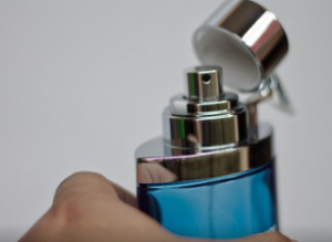 Hand holding an open blue and silver bottle of perfume.