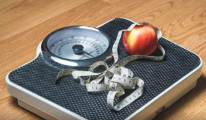 Image of a bathroom scale with an apple and a measuring tape on it.