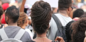 Rear view of several races of people and one lady with a big dreadlocks bun.