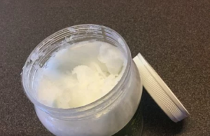 A jar of white, creamy coconut oil with the cover resting on the side.