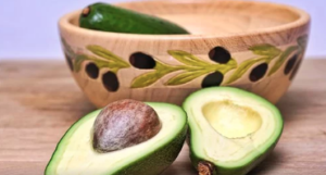 A beige decorated ceramic bowl with an avocado inside and an avocado cut in half beside it.