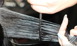 A hand cutting a section of black hair.