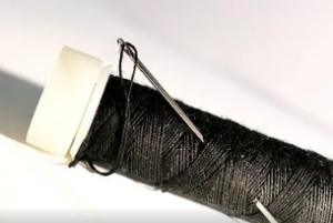 Spool of black thread with a needle pushed through.