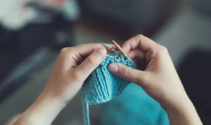 Two hands knitting an aqua blue project.