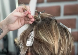 A hand applying light-blonde foil highlights.
