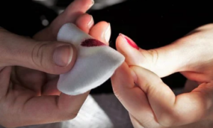 Female hands removing red nail polish with a cotton ball.