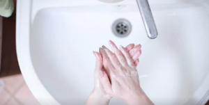 Person's hands being washed with soap over a sink.