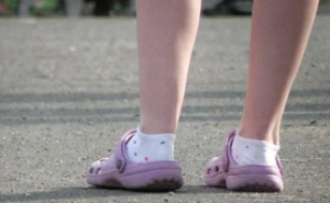 Legs of a person wearing mauve croc sandals and white socks with coloured dots.