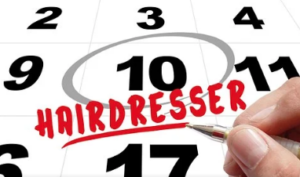 Hand with pen writing hairdresser below circled appointment on desk calendar.