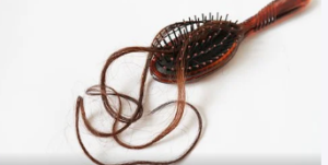 A brown vented brush with strands of long, copper hair.