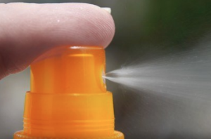 A finger pressing the nozzle of an orange spray bottle.