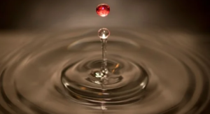 A red coloured drop of water falling in a puddle.