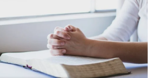 Person with hands clasped on an open bible.