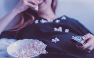 Female eating popcorn and using television remote.