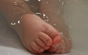 A pair of baby's feet in a bath with one foot sticking out of the water.
