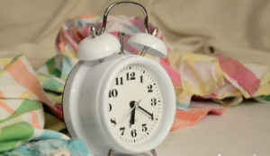 A white alarm clock with multicoloured cloth in the background.