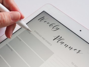 Fingers with a white pen writing on a planner.