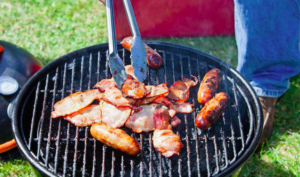 Person cooking sausages on small barbeque.