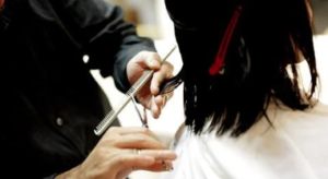 Person holding scissors and a comb, cutting the back of someone's hair.