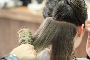 A hand blow drying long, medium-brown hair, with a round brush.