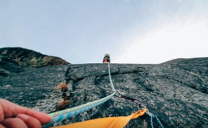 Person on top of a mountain holding the line for their partner to come up.