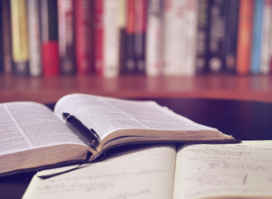 Two open books, one with a pen in the middle, in a library.