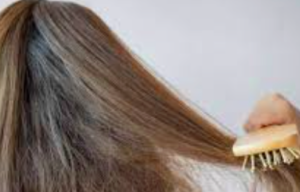 A person with long, light brown hair brushing with a wooden paddle brush.