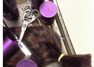 A bundle of cut reddish-brown hair on a tray with scissors and hot rollers.