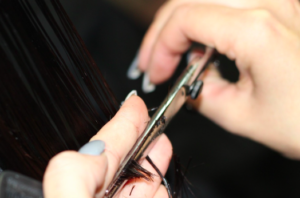 A hand holding hair while cutting the ends with a pair of scissors.