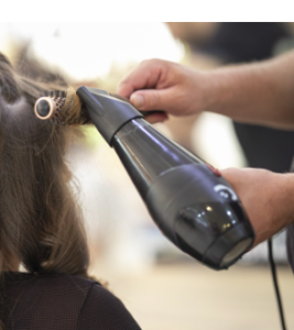 Hands with a black blowdryer, drying the hair with a round brush.