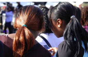 Two teenage girls, one with copper and the other with black straight hair with heads together talking.