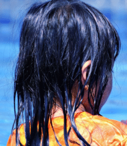The side view of a child with soaked long, black hair on a beach.