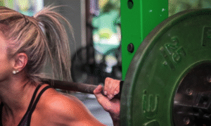 Female with hair in ponytail lifting green-colored weights.