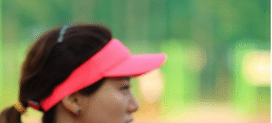 Female with hair in ponytail wearing a salmon-colored visor hat.
