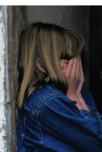 A female with striped blonde hair hiding her face in her hands.