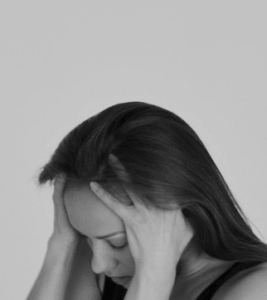 A woman in black and white holding her head in both hands, eyes closed
