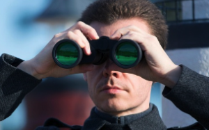 A white male looking in a distance with binoculars.