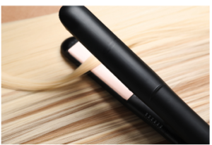 A black flat iron resting on a section of straightened blonde hair