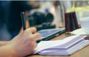 A person's hand writing in a book on a desk.
