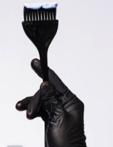 A gloved hand holding a tint brush loaded with hair colour